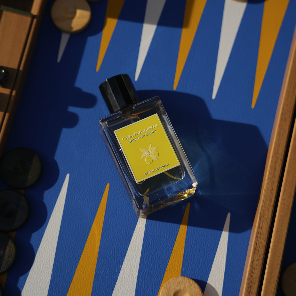 Casa Far Niente Crema di Capri Flakon mit gelber Plakette, Lifestyle-Aufnahme, liegend auf Backgammon-Brett mit blauem Leder